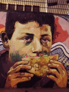 [The wall of Mohammed Mahmoud Street, a few meters from the entrance of the gate of the American University in Cairo. A poor child, (most probably a street child) eating a falafel sandwich. Captured 25 November 2013]