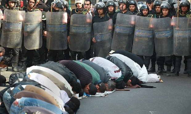 Locals pray in the street in front of The l-Istiqama Mosque watched by riot police in Giza on 28 January 2011 in Cairo, Egypt. Photograph: Peter Macdiarmid/Getty Images